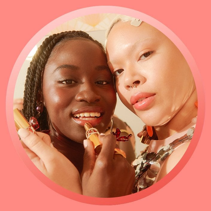two people leaning on each other applying lipstick