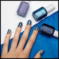 hand with nails painted blue poses next to three bottles of blue nail polish