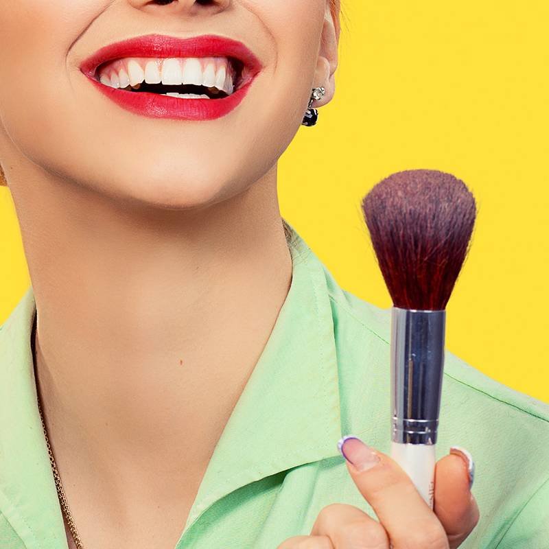 person wearing red lipstick and holding makeup brush