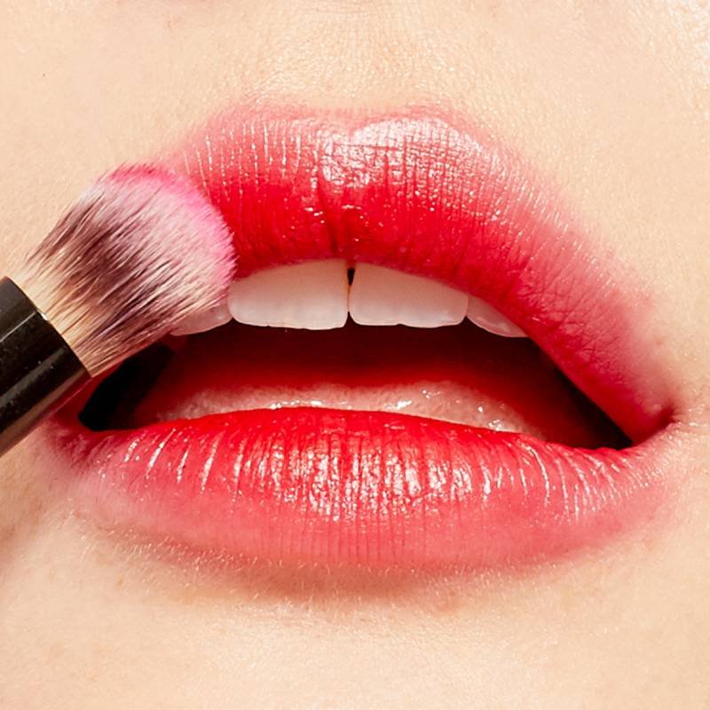 close-up of makeup brush applying red lipstick to lips
