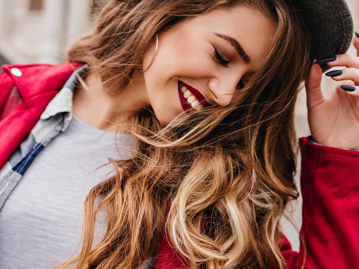 person with blonde highlights in hair smiling and wearing red lipstick
