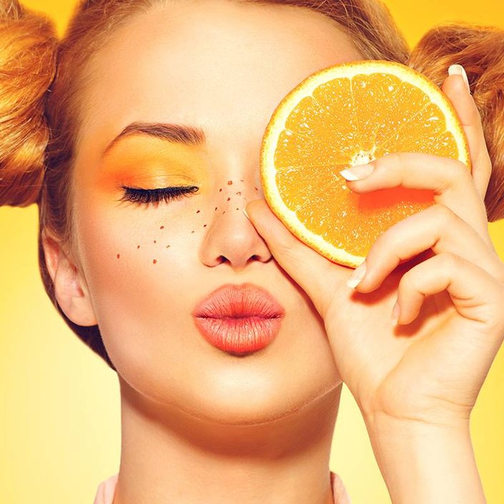person wearing orange eyeshadow holding orange slice up to eye