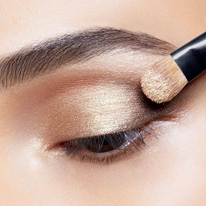 makeup brush applying gold eyeshadow to eyelid