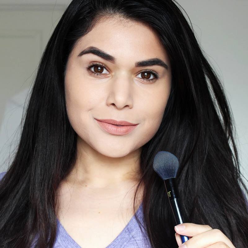 person with long dark brown hair holding a makeup brush