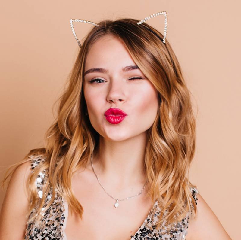 person wearing a rhinestone cat-ear headband, red lipstick, and a sequin top
