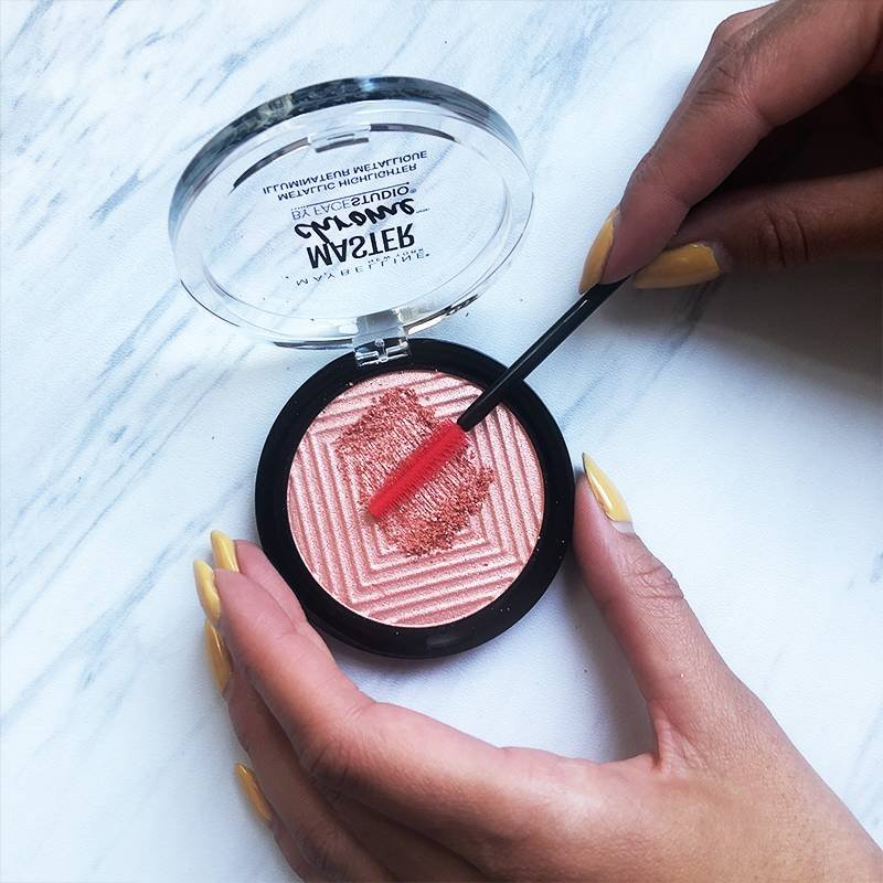 person holding a spoolie to pressed powder compact