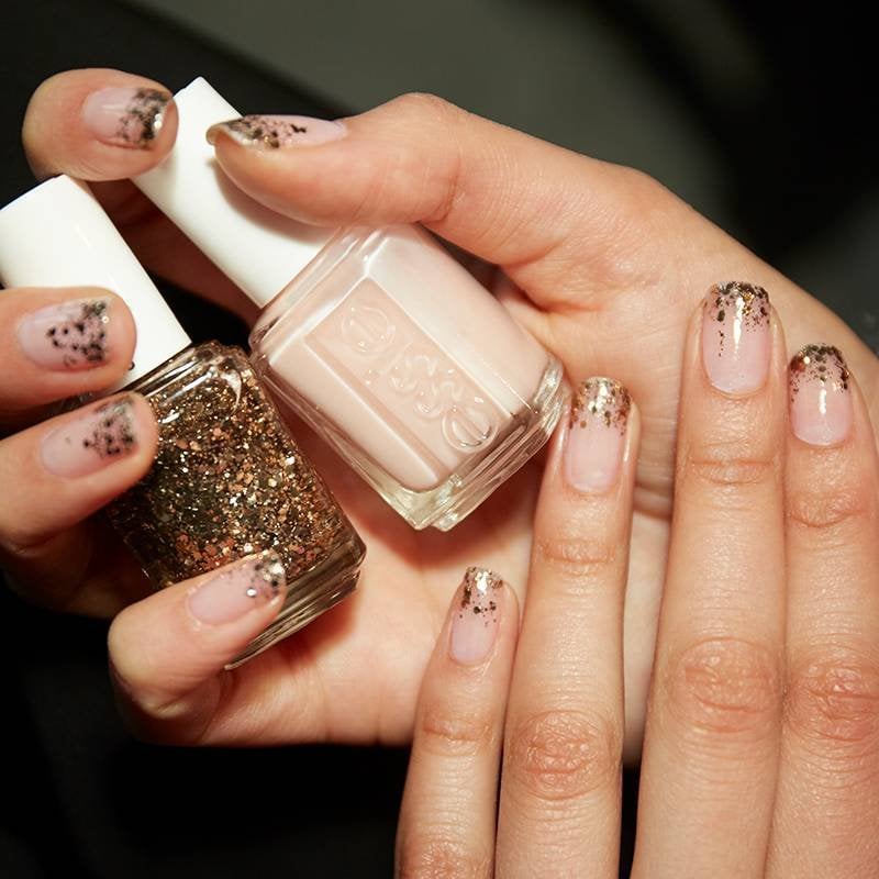 hands with gold glitter on nails holding essie nail polish
