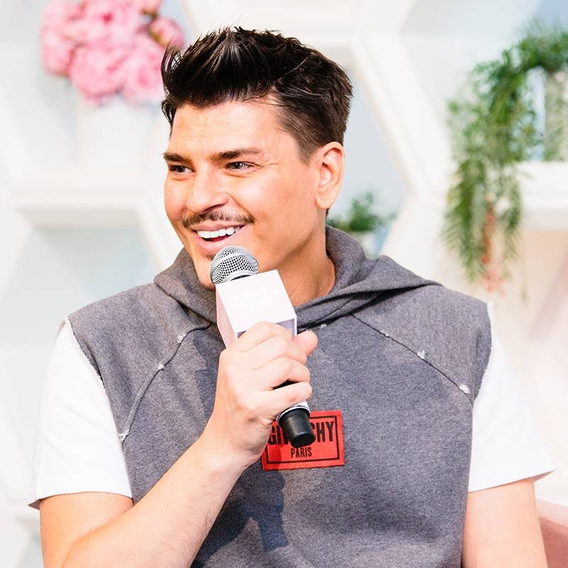 person smiling and holding mic on stage at beauty summit