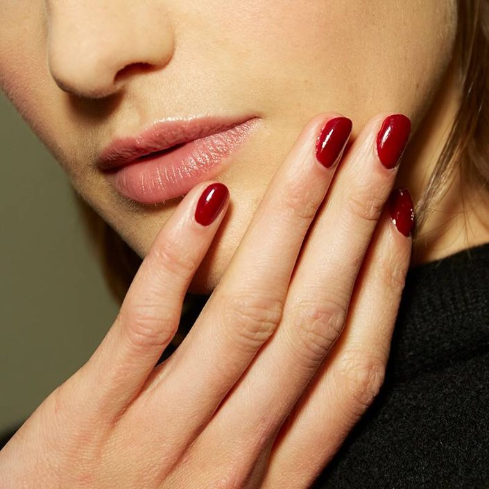 hand with nails painted dark red resting on person's chin