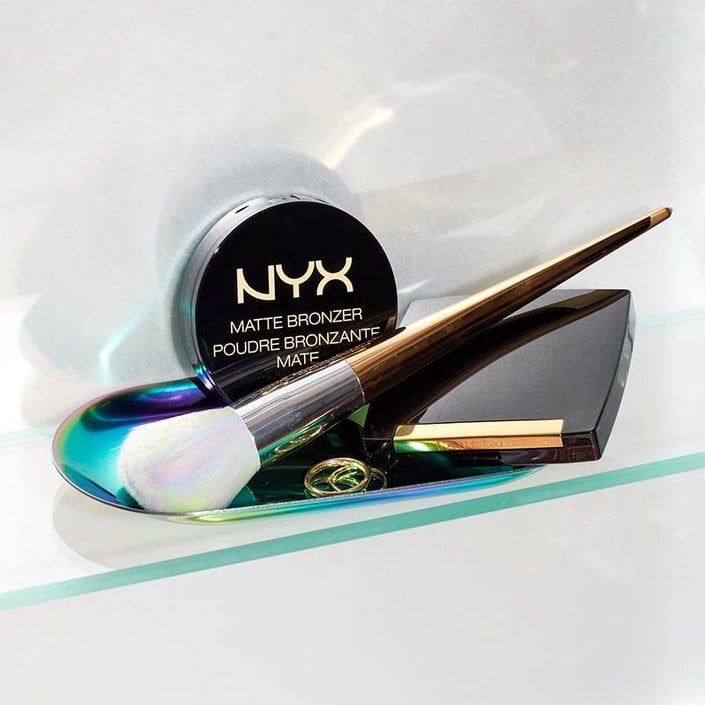 NYX Professional Makeup Matte Bronzer, Lancôme Dual Finish Highlighter, and a makeup brush on a tray with gold rings