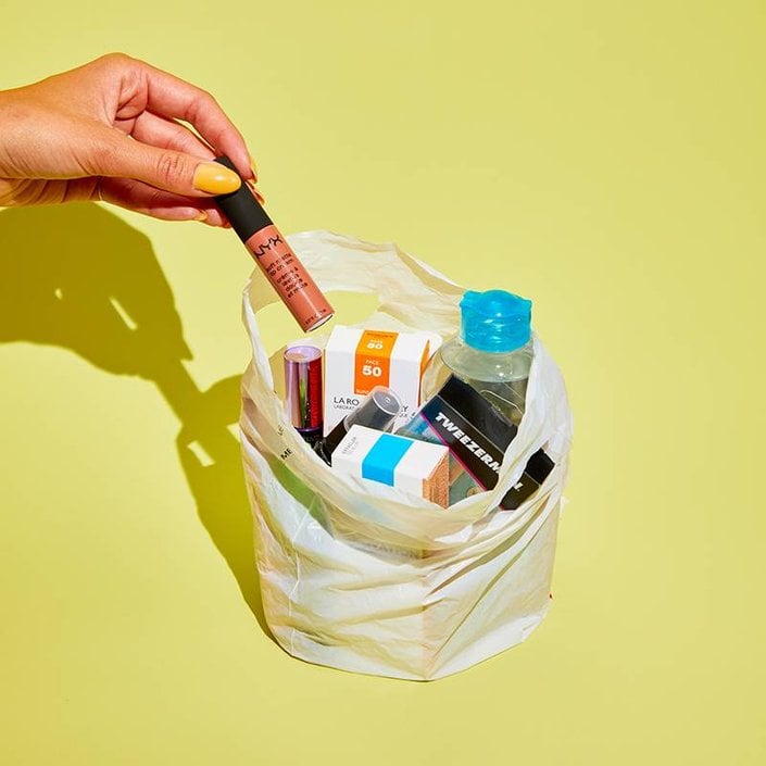 hand holding NYX Professional Makeup Soft Matte Lip Cream over shopping bag filled with beauty products