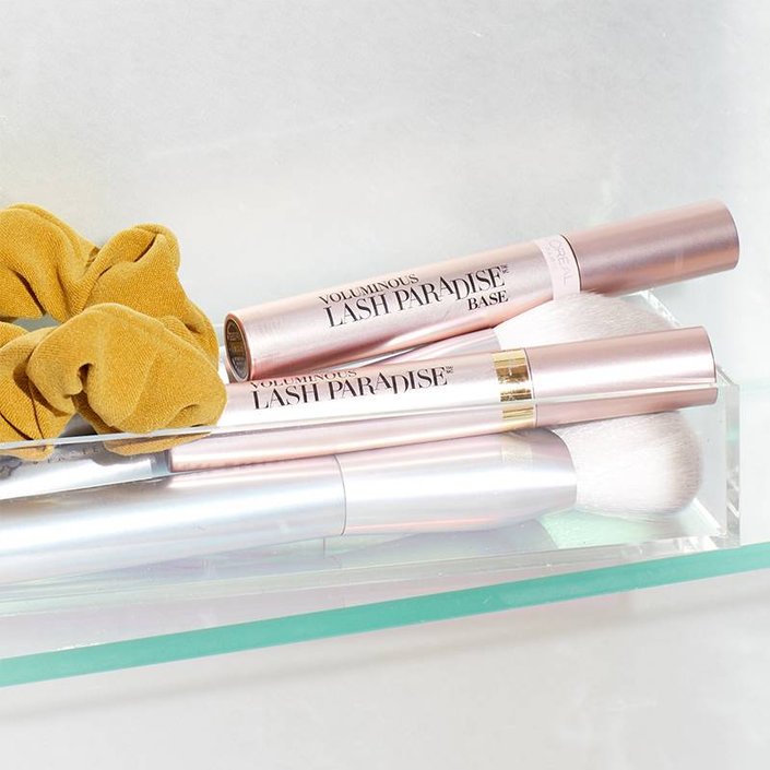 L’Oréal Voluminous Lash Paradise Primer, makeup brushes, and yellow hair scrunchie in glass container