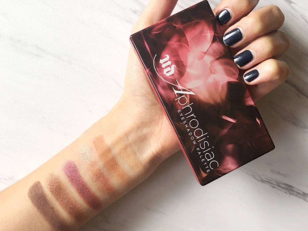 hand holding Urban Decay Aphrodisiac Palette with swatches on arm