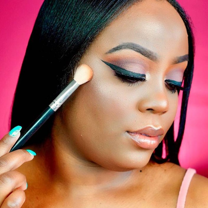 person applying highlighter to cheekbone with makeup brush