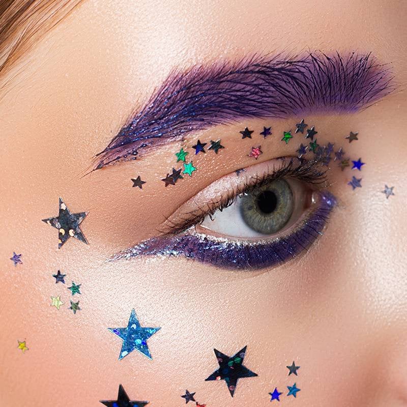 person wearing purple makeup on eyebrow and under eye, and stickers on face