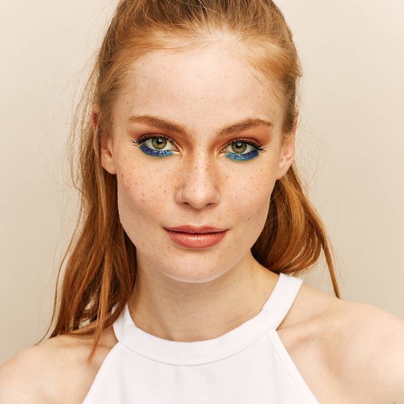 person with red hair and freckles wearing blue eyeshadow under eye