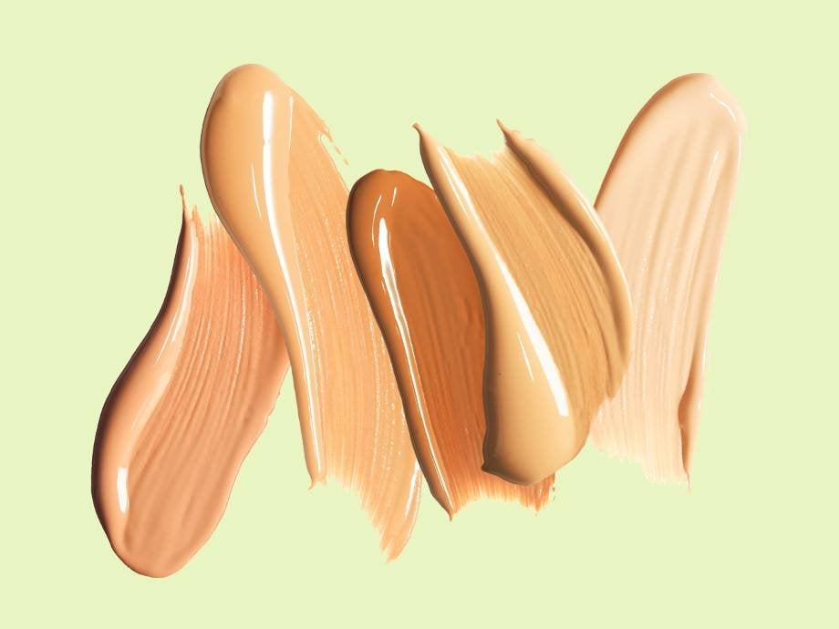 Swatches of different shades of liquid foundation on a green background.