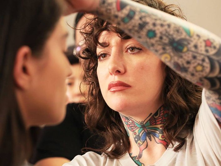 person with tattoos on neck and arm doing someone's makeup