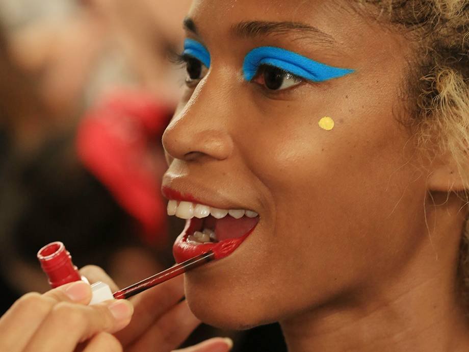 hand applying red liquid lipstick to model wearing blue eyeshadow