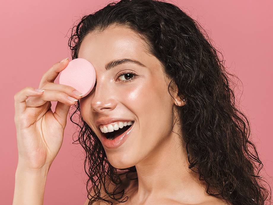 person holding pink round makeup sponge to eye