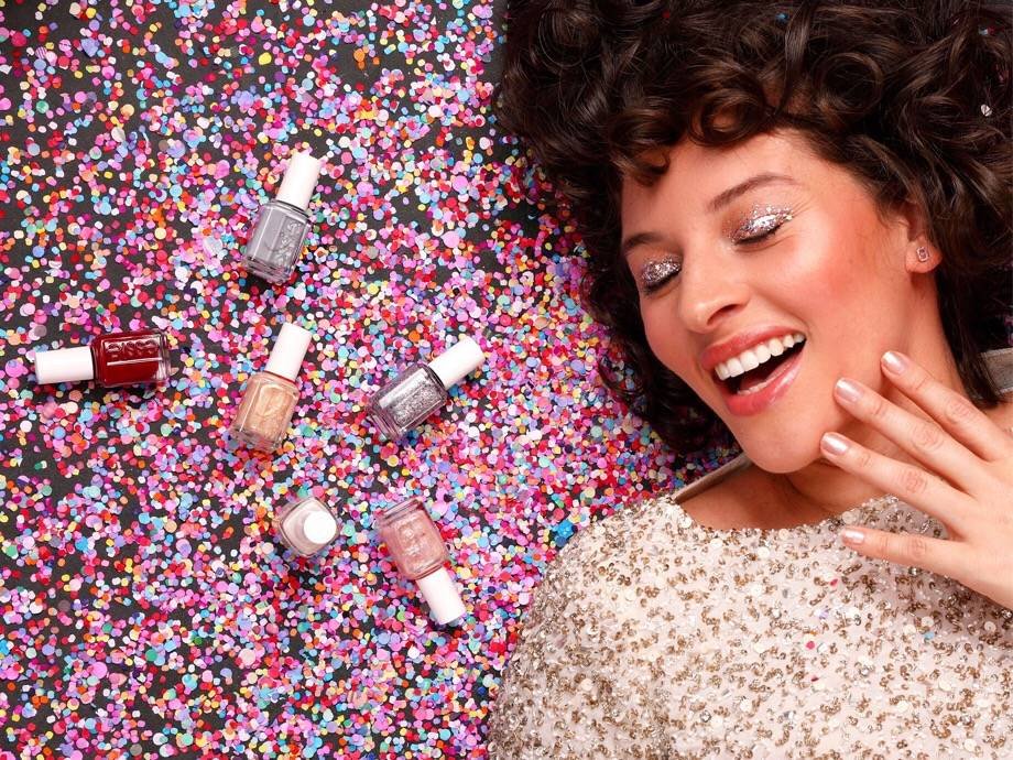 person wearing glitter eyeshadow and laying in confetti with essie nail polish bottles