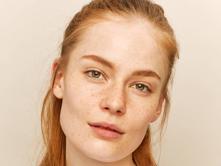 person with red hair and freckles wearing barely there makeup