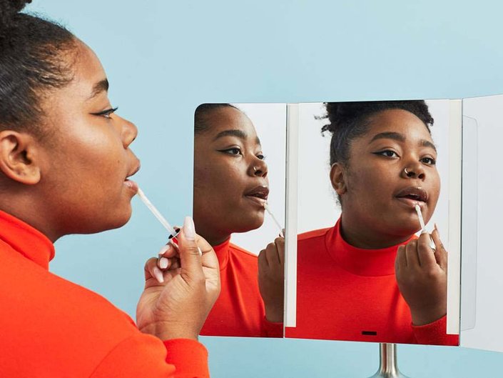 person applying glossy lip balm in mirror