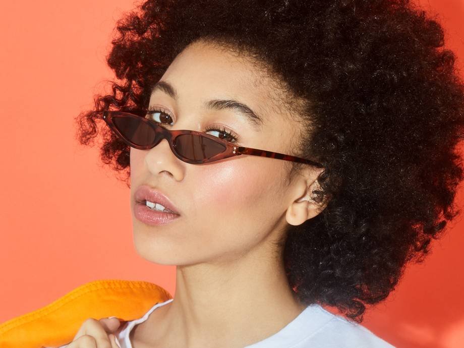 person with naturally curly hair in afro wearing monochromatic pink makeup and sunglasses