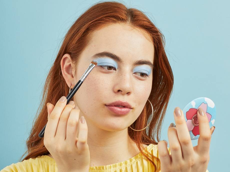 person applying light blue eyeshadow in a compact mirror