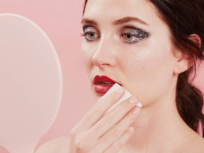 person wearing silver glitter eye makeup and red lipstick and holding cotton pad to mouth