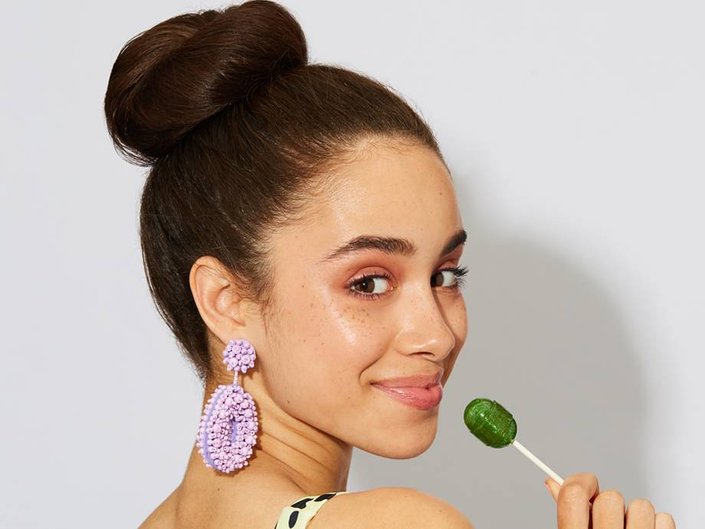 person with high bun holding a green lollipop