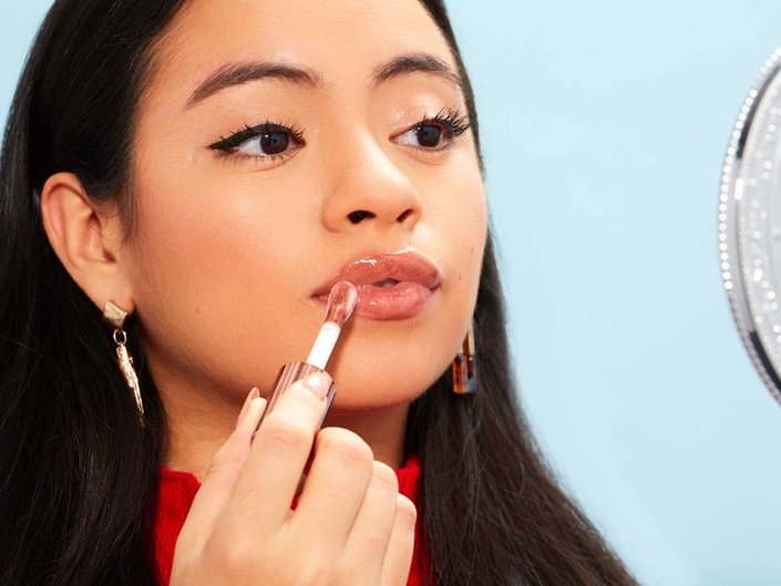person applying lip gloss in handheld mirror