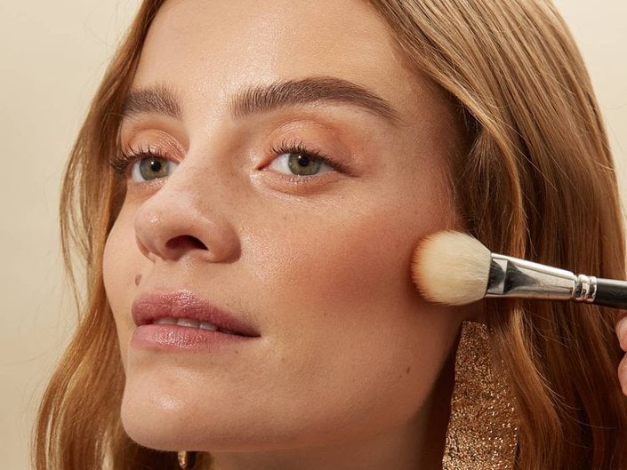 person applying blush to cheek with makeup brush