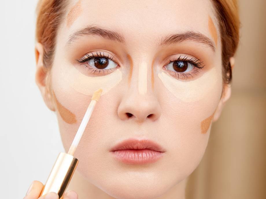 person applying concealer to face while wearing concealer swatches