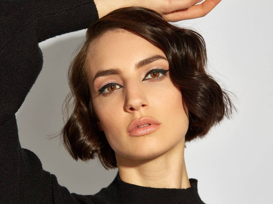 person with black eyeliner and short brown hair on a neutral background