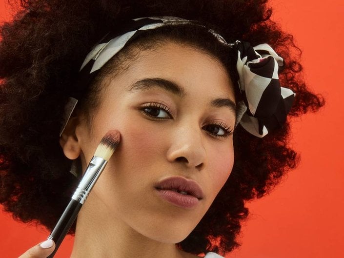 person applying blush to cheek with makeup brush