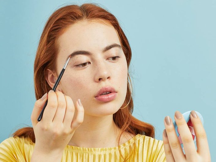 person applying brow pomade through a compact mirror