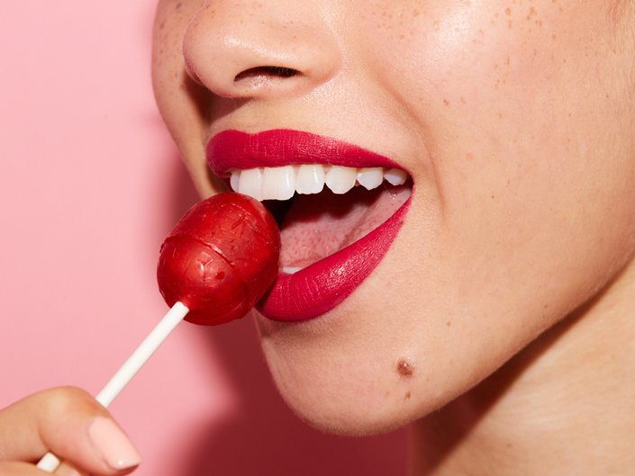 person wearing red lipstick and holding red lollipop to mouth
