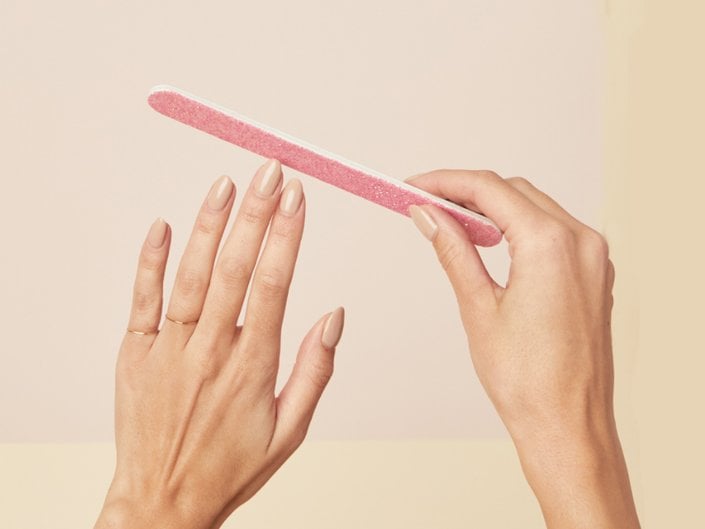Person with manicured nails painted nude holding up a pink nail file