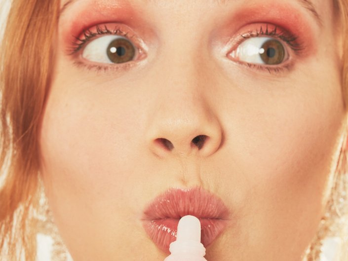 person wearing pink monochromatic makeup and holding lip gloss to mouth