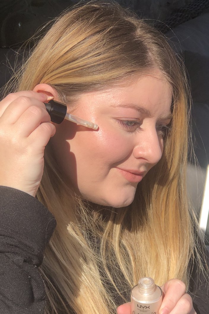 person holding dropper filled with highlighter to cheek
