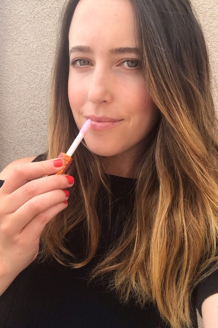 person applying lip gloss to lips