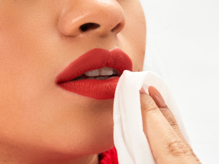 person wearing red lipstick and holding makeup remover wipe to mouth