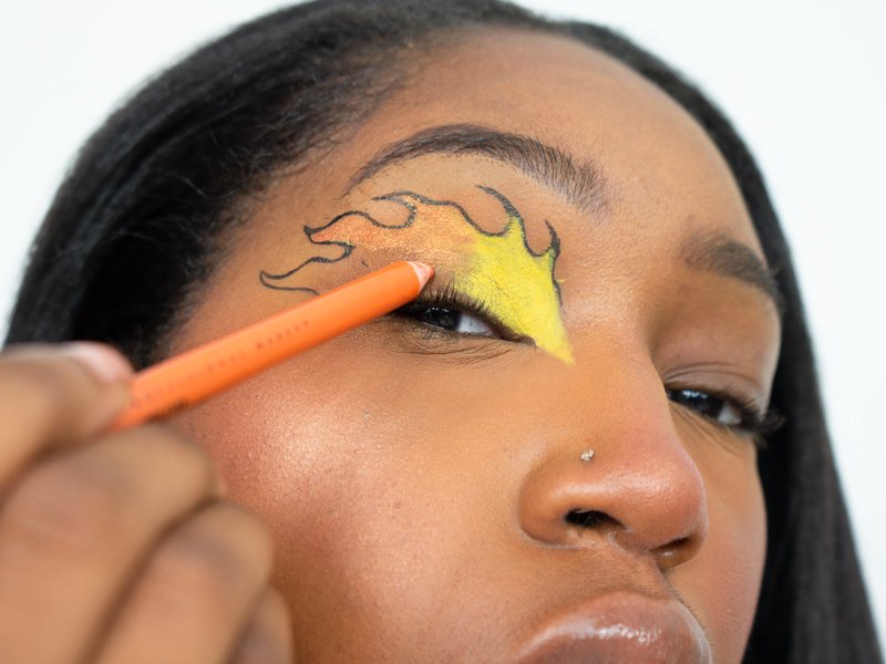 person applying orange eyeliner to eyelid