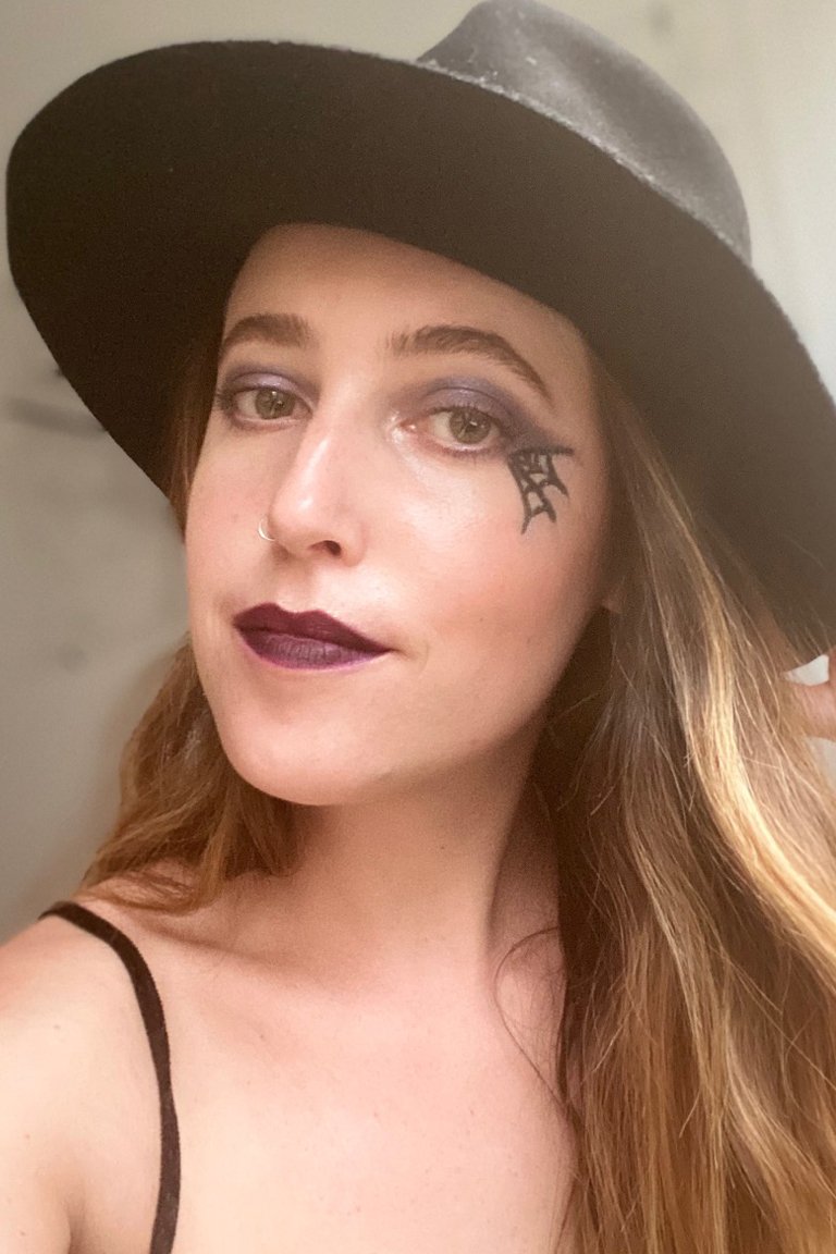 person wearing a witch hat, spider web eye makeup and deep red lipstick