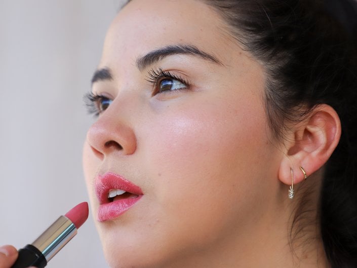 person wearing pink lipstick and holding lipstick to mouth