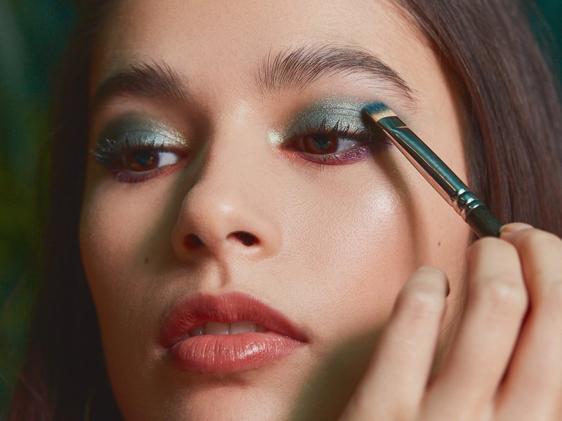person applying green shadow to eyelid with makeup brush