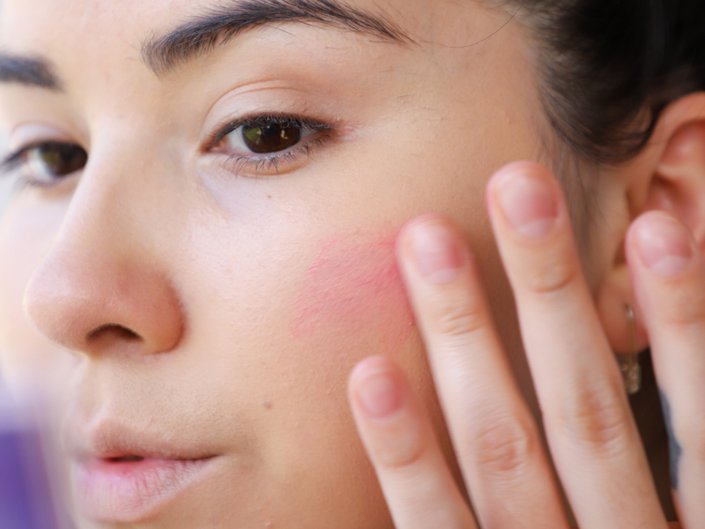 person applying cream blush to cheek with finger