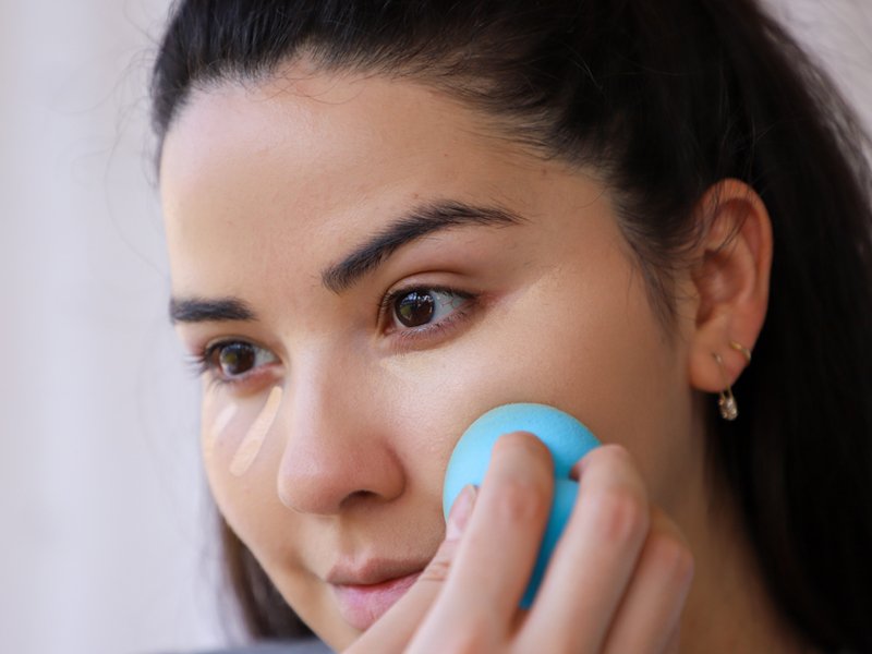 person applying makeup to face with makeup sponge