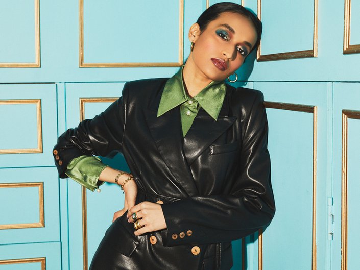 person wearing gold glitter and blue eyeshadow, nude lipstick, a green shirt, and a black leather jacket